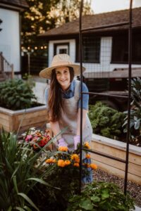 Woman in sun hat gardening in backyard with flowers and vegetables on a sunny day in Georgetown Texas